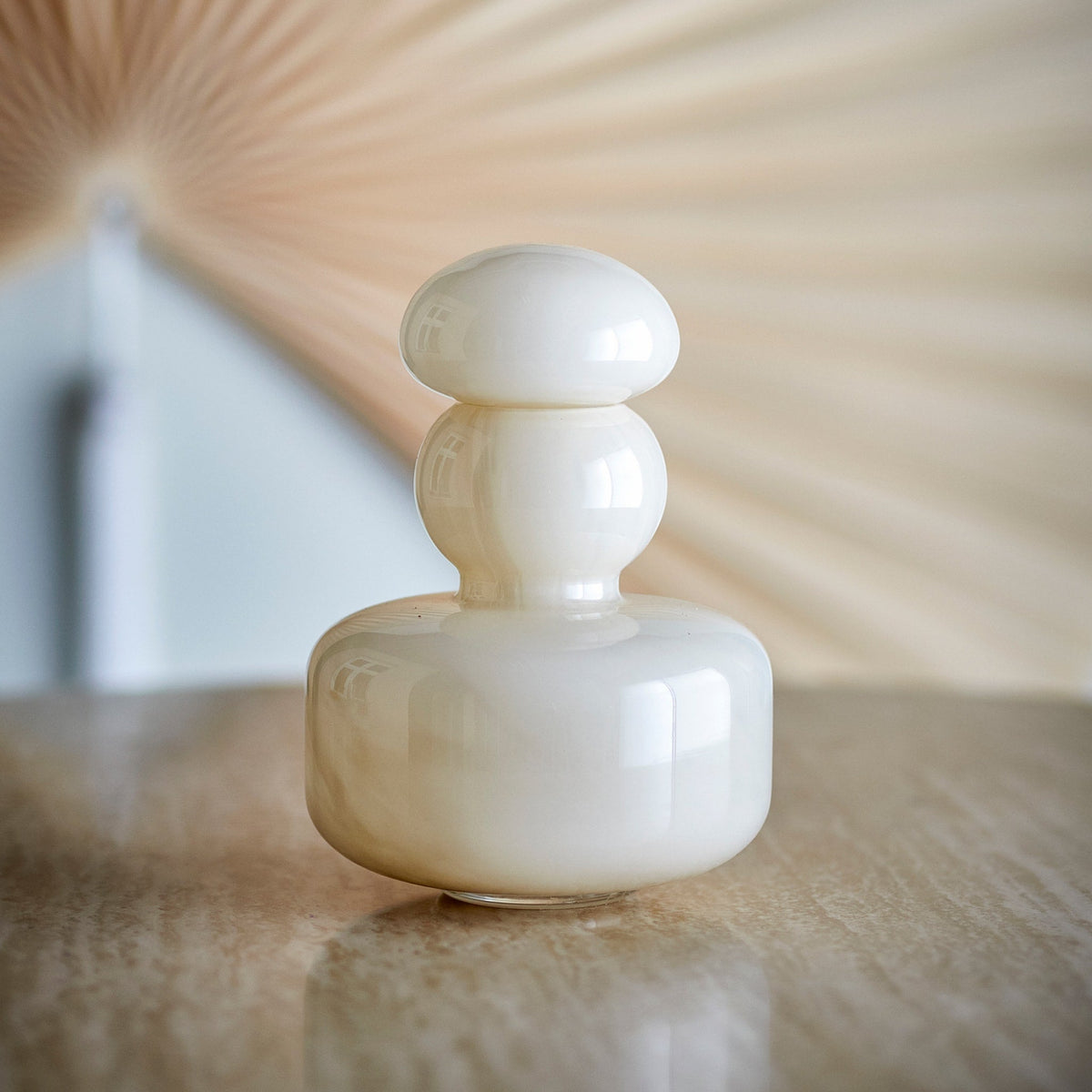 Gros plan du vase Cynthia en verre beige, fermé avec son couvercle sur une table.